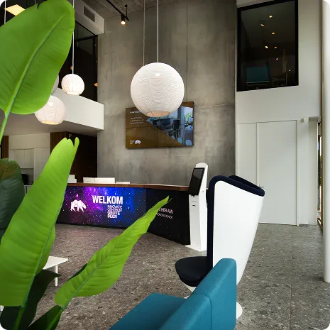 Moderne receptie met verlichte balie met welkom-tekst, grote groene planten en designstoelen in een strak interieur.