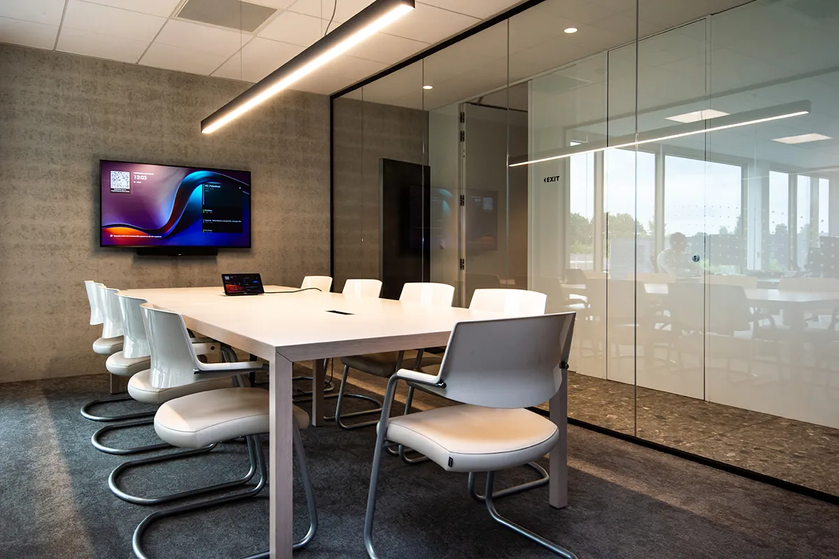 Middelgrote vergaderruimte met glazen wanden, een tafel met zes stoelen en een scherm aan de muur.