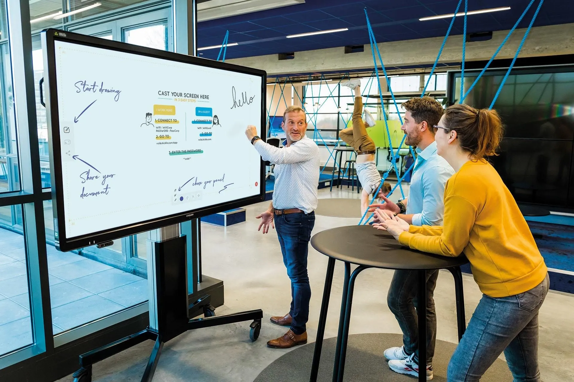 Drie collega's overleggen bij een groot digitaal whiteboard in een modern kantoor.