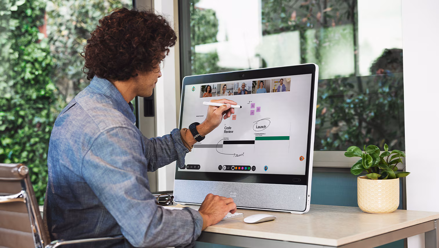Een man die met een stylus op een touchscreen-computer schrijft tijdens een videogesprek met vijf mensen aan de bovenkant van het scherm.