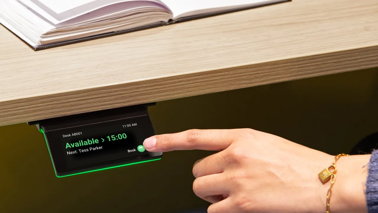 Een hand die op een touchscreen met bureauboekingsinformatie tikt, met tekst 'Beschikbaar > 15:00' en 'Volgende: Tess Parker'.