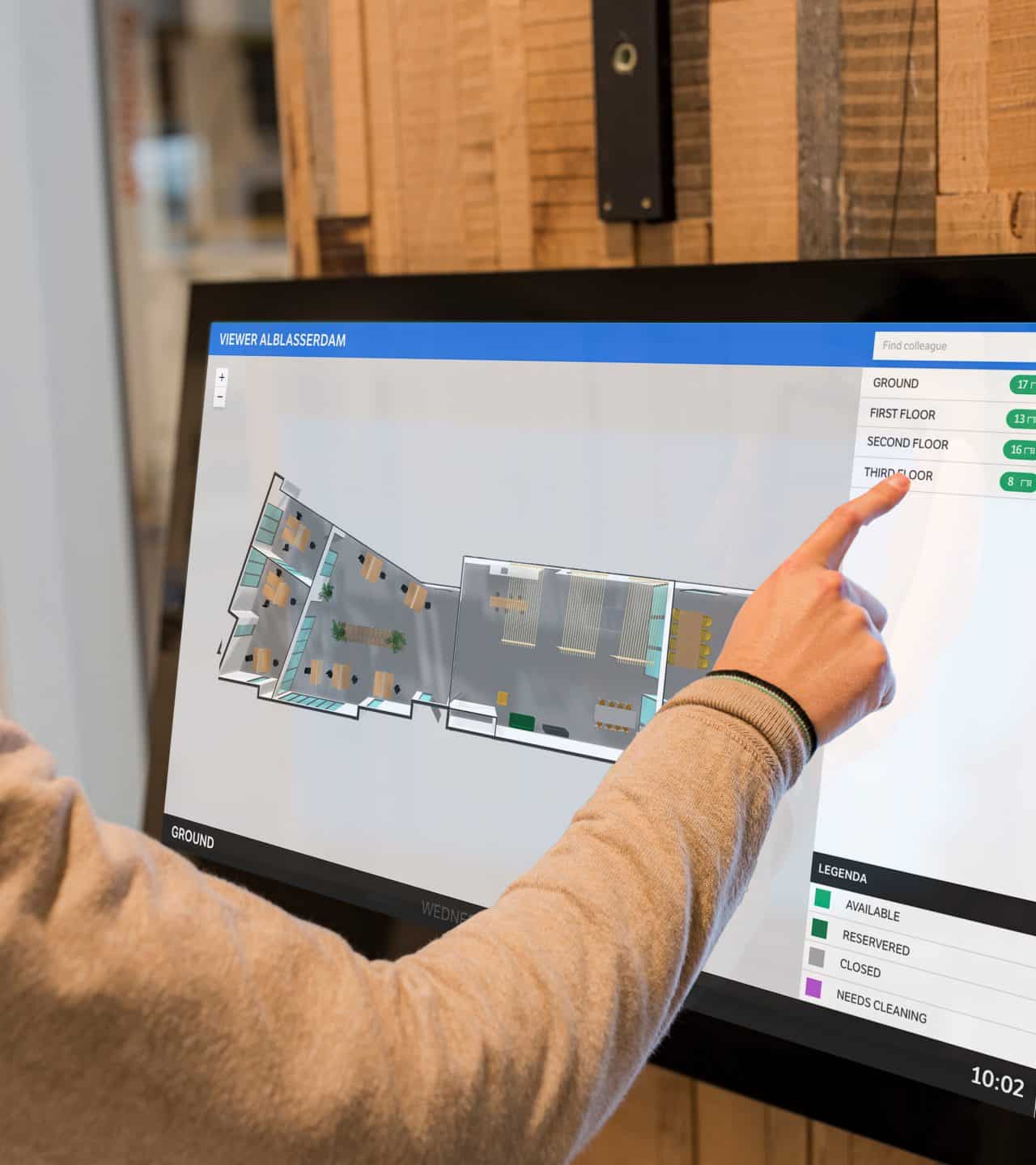 Hand wijst naar interactieve plattegrond op een scherm met kantoorindeling en beschikbare verdiepingen.