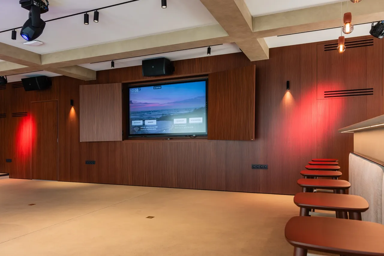 Moderne conferentieruimte met houten wanden, een groot scherm en een rij rode stoelen langs de rechtermuur.