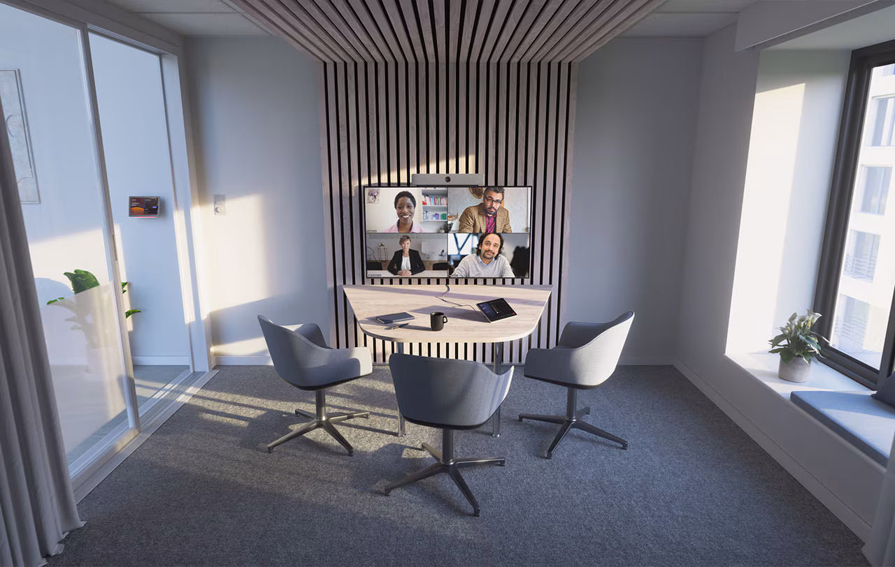 Kleine vergaderruimte met drie stoelen rond een tafel en een scherm voor videoconferentie met vier mensen.