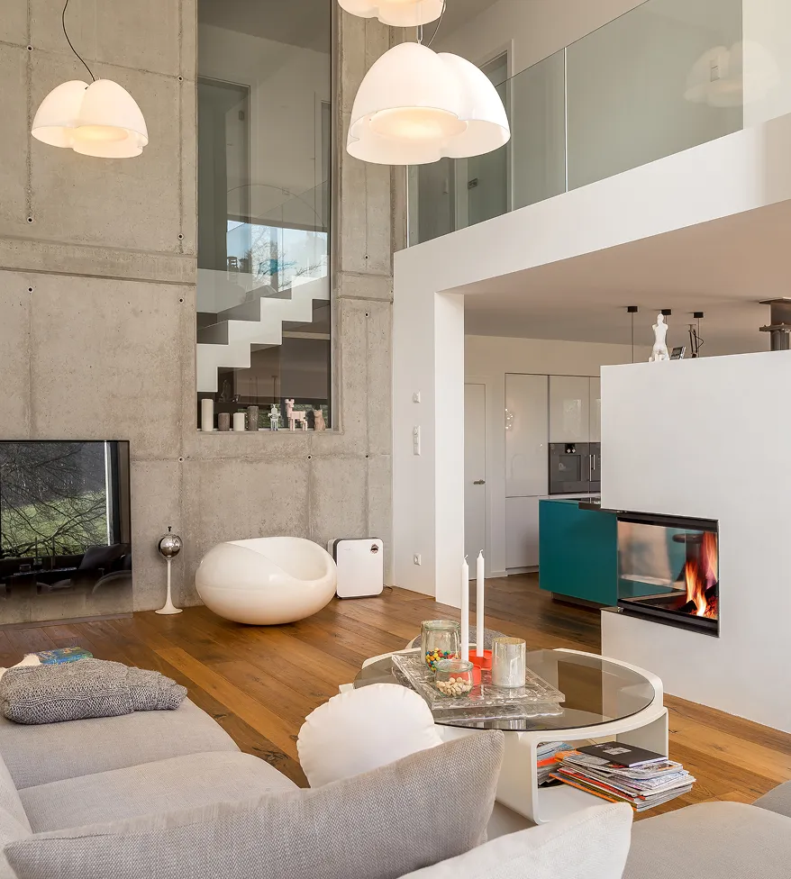 Moderner Wohnzimmerinterior mit Betonwand, weißem Kamin, Glas-Couchtisch und grauem Sofa auf Holzboden.