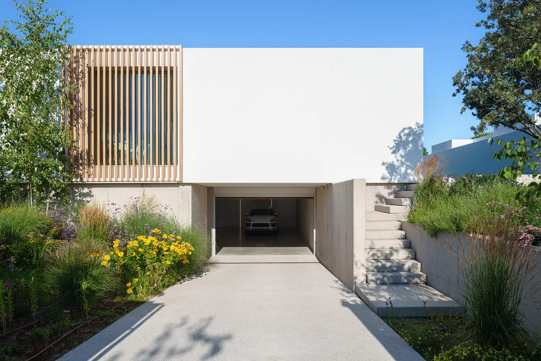 Modernes Haus mit weißer Fassade, einer offenen Garage mit einem Auto und einem umliegenden Garten mit bunten Blumen.