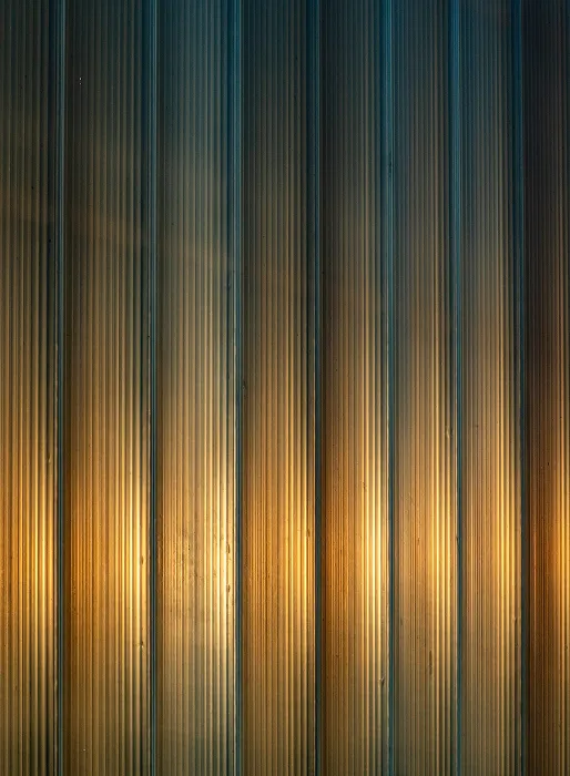 Vertikaler Blick auf beleuchtete, geriffelte Metallpaneele in warmem Licht.
