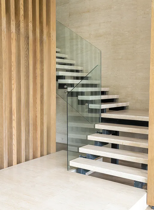 Moderner Innenraum mit einer Treppe aus hellen Steinplatten und Glasgeländer, daneben vertikale Holzpaneele.