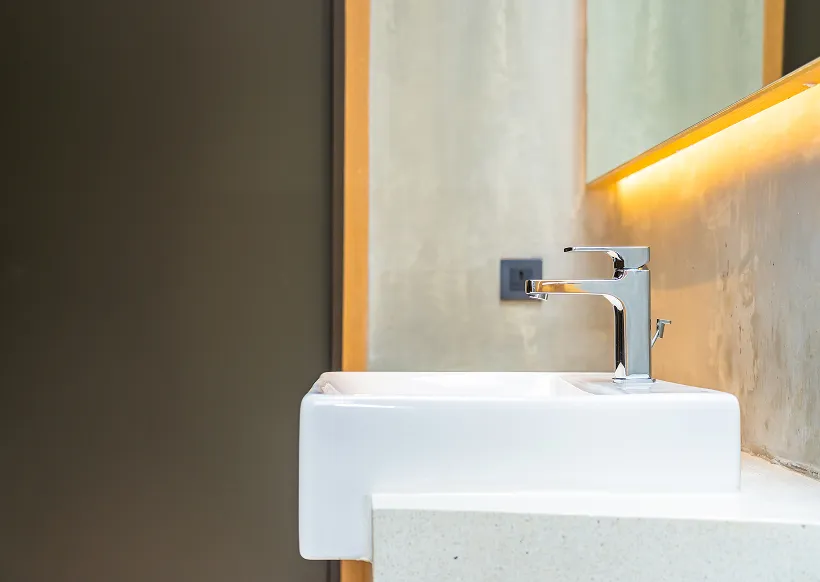 Moderner weißer Waschtisch mit verchromtem Wasserhahn und beleuchtetem Spiegel in einem Badezimmer.