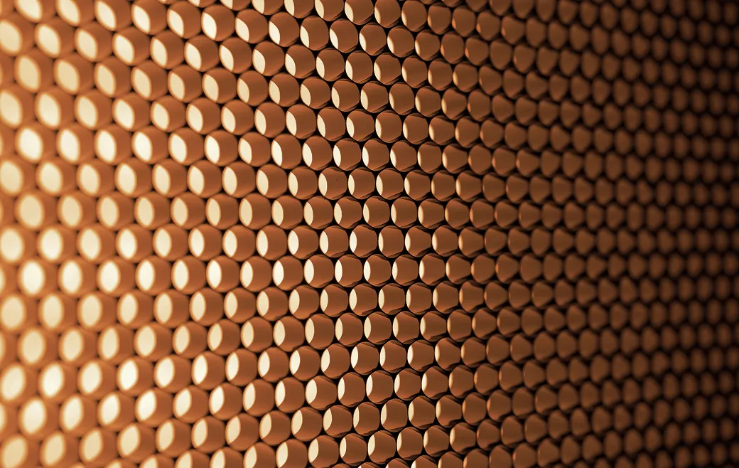 Nahaufnahme einer Musterwand aus kupferfarbenen, runden, hohlen Zylindern in einem regelmäßigen Raster.