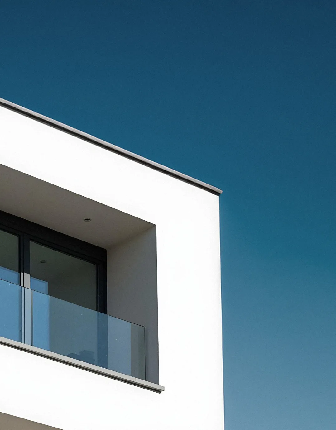 Moderner Balkon mit Glasschutz an einem weißen Gebäude vor klarem blauem Himmel.