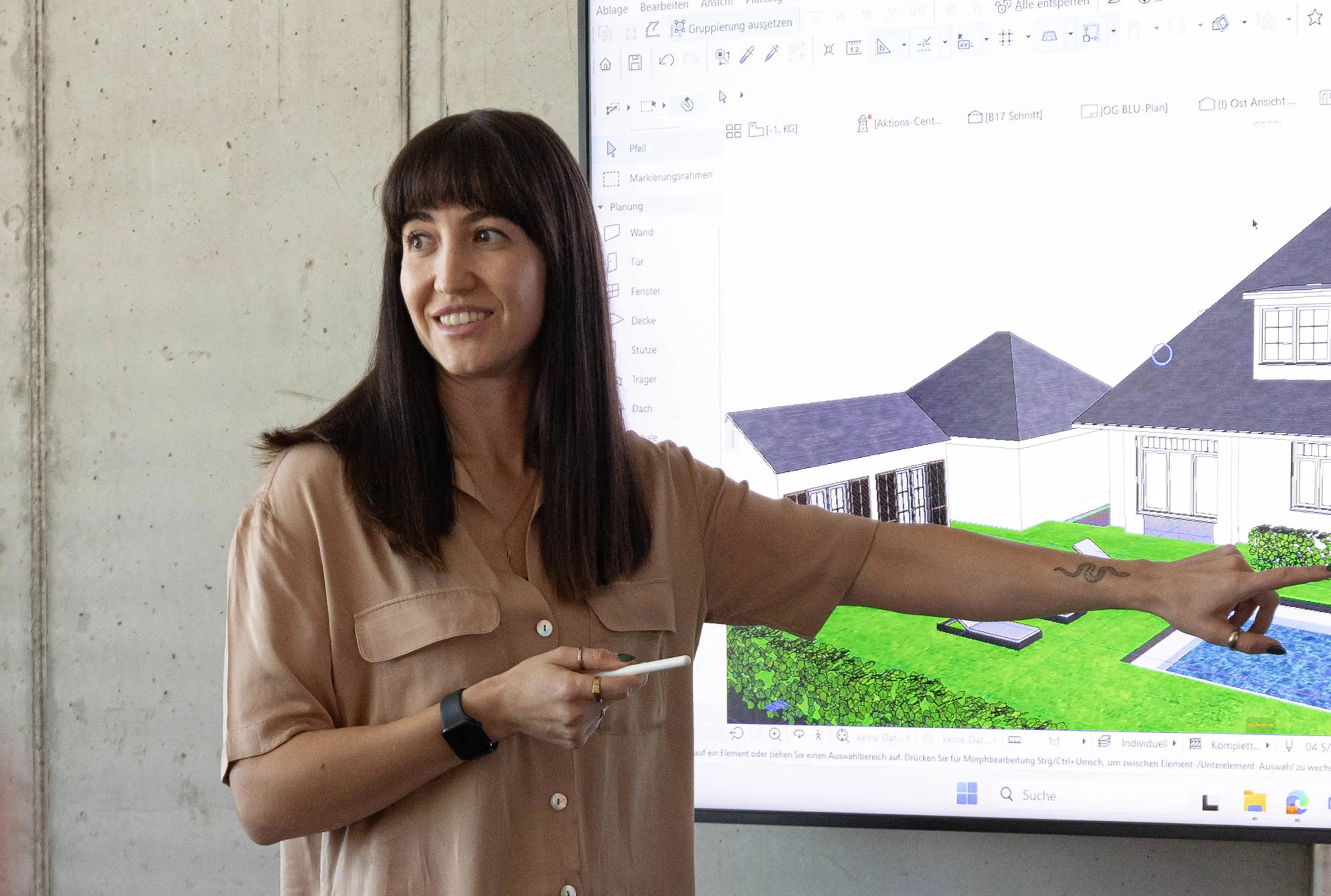 Frau zeigt auf einem Bildschirm ein 3D-Modell eines Hauses mit Garten und Pool.