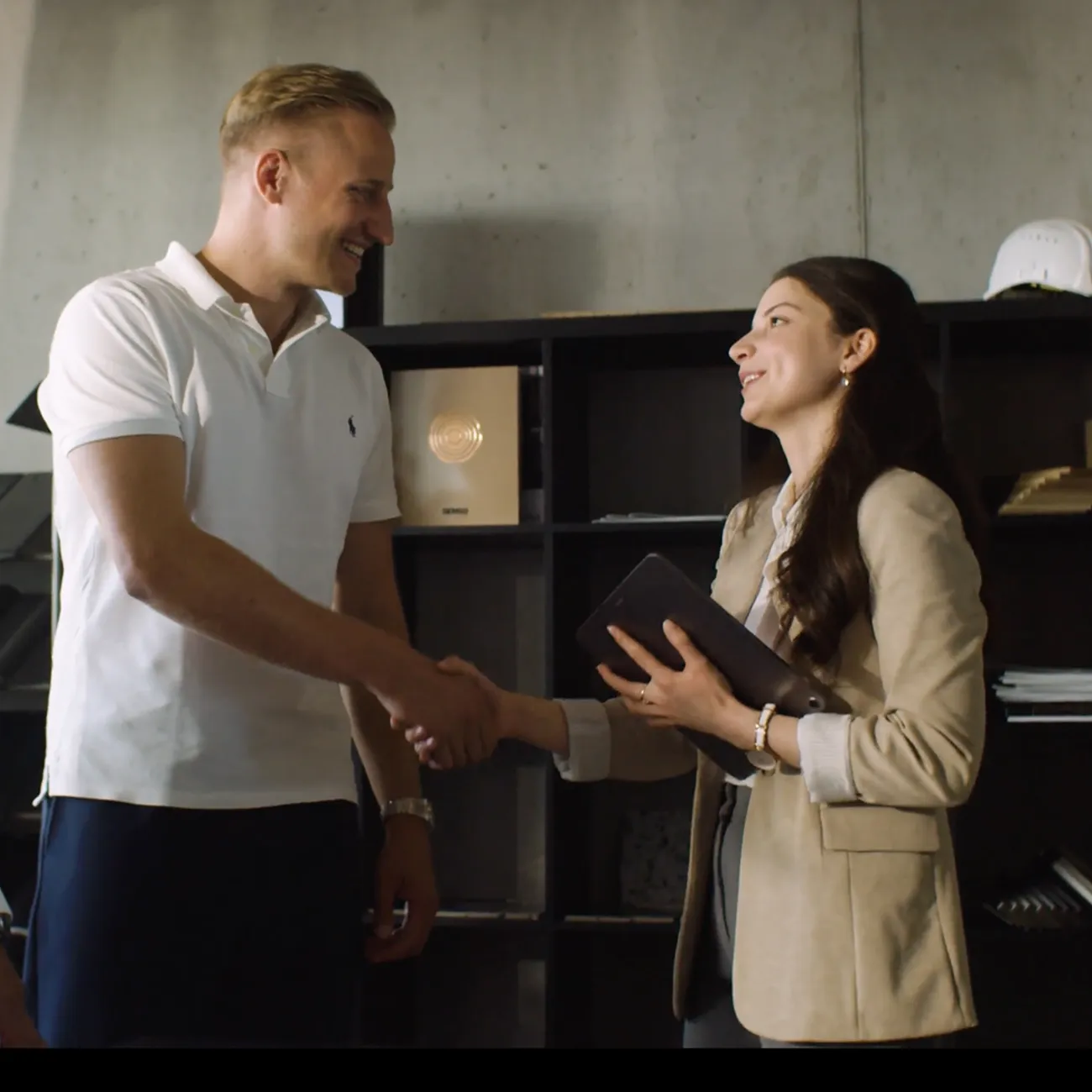 Ein Mann und eine Frau schütteln sich lächelnd die Hand in einem modernen Büro.