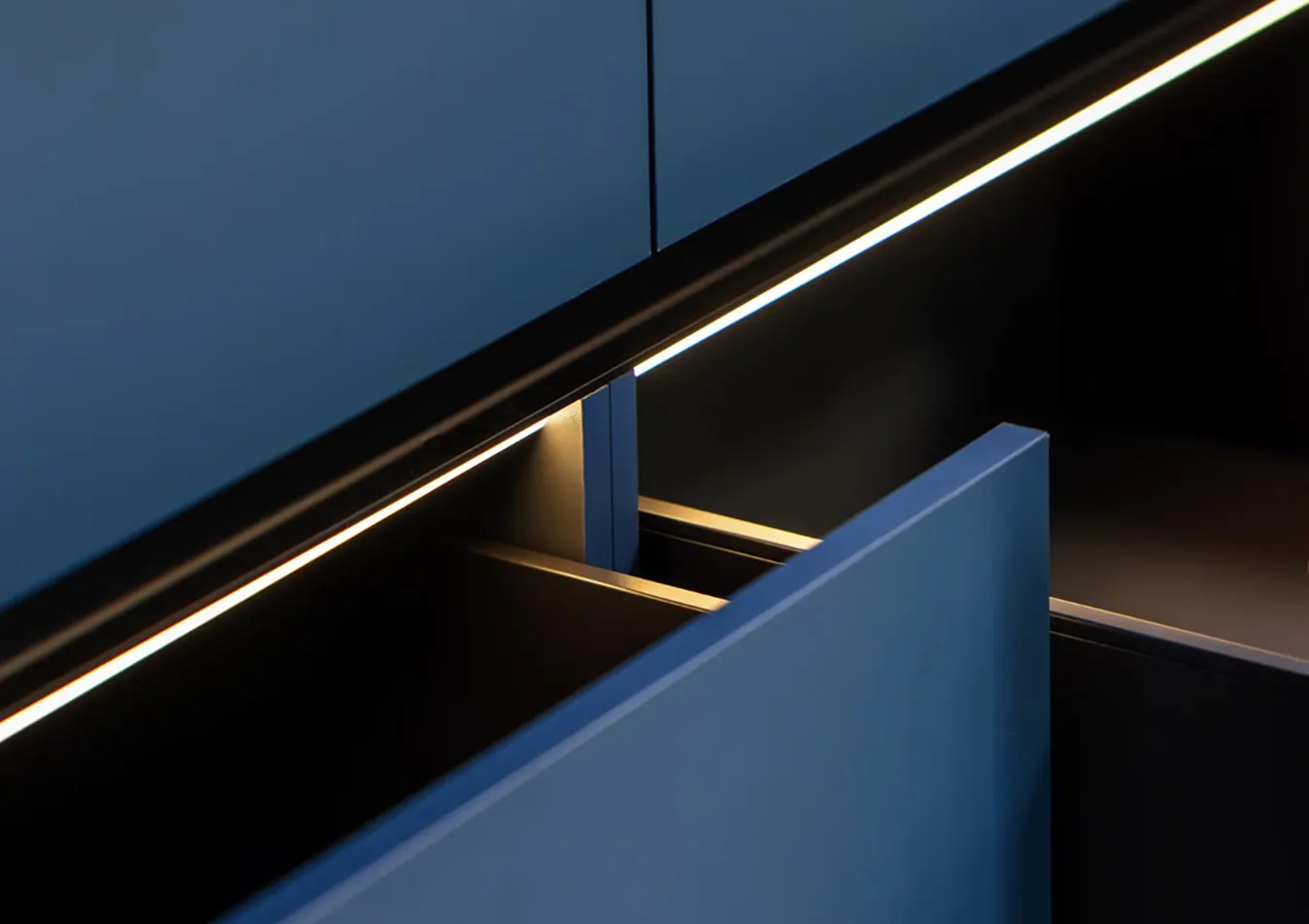 Nahaufnahme einer geöffneten blauen Küchenschublade mit integrierter indirekter Beleuchtung darunter.