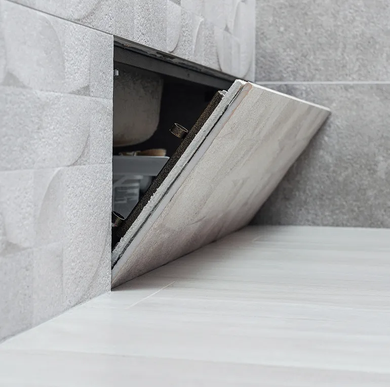 Geöffnete Bodentür mit grauen Fliesen, die Zugang zu einem versteckten Fach im Boden bietet.