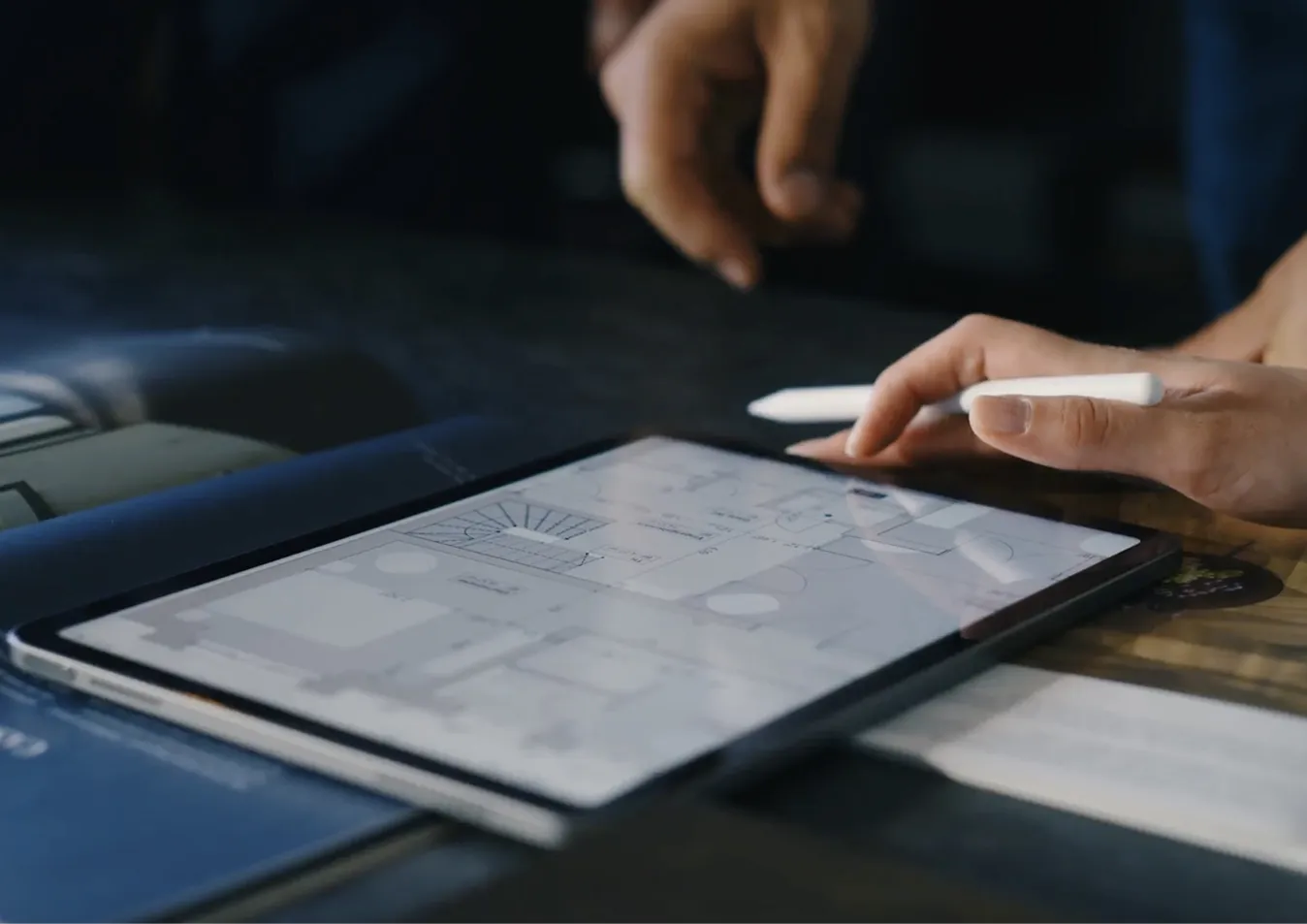 Hand hält einen weißen Stylus über ein Tablet mit einem digitalen Architekturgrundriss.