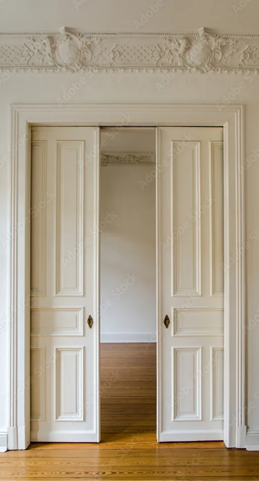 Offene weiße Doppeltüren mit dekorativen Paneelen führen zu einem leeren Raum mit hölzernem Boden und Stuckdecke.