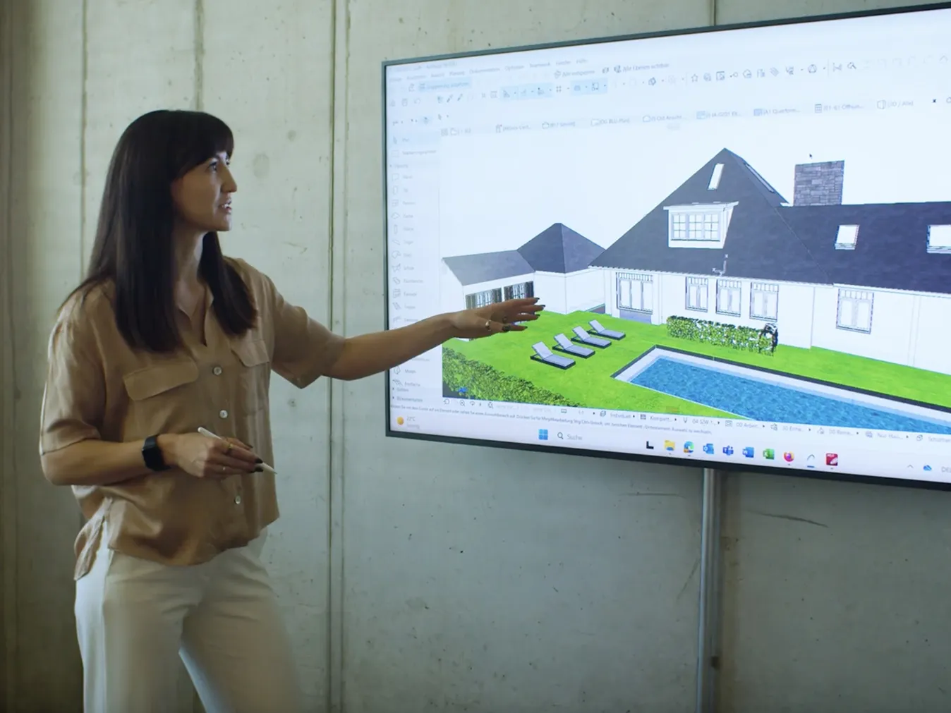Frau präsentiert auf einem Bildschirm ein 3D-Modell eines Hauses mit Garten, Pool und Sonnenliegen.