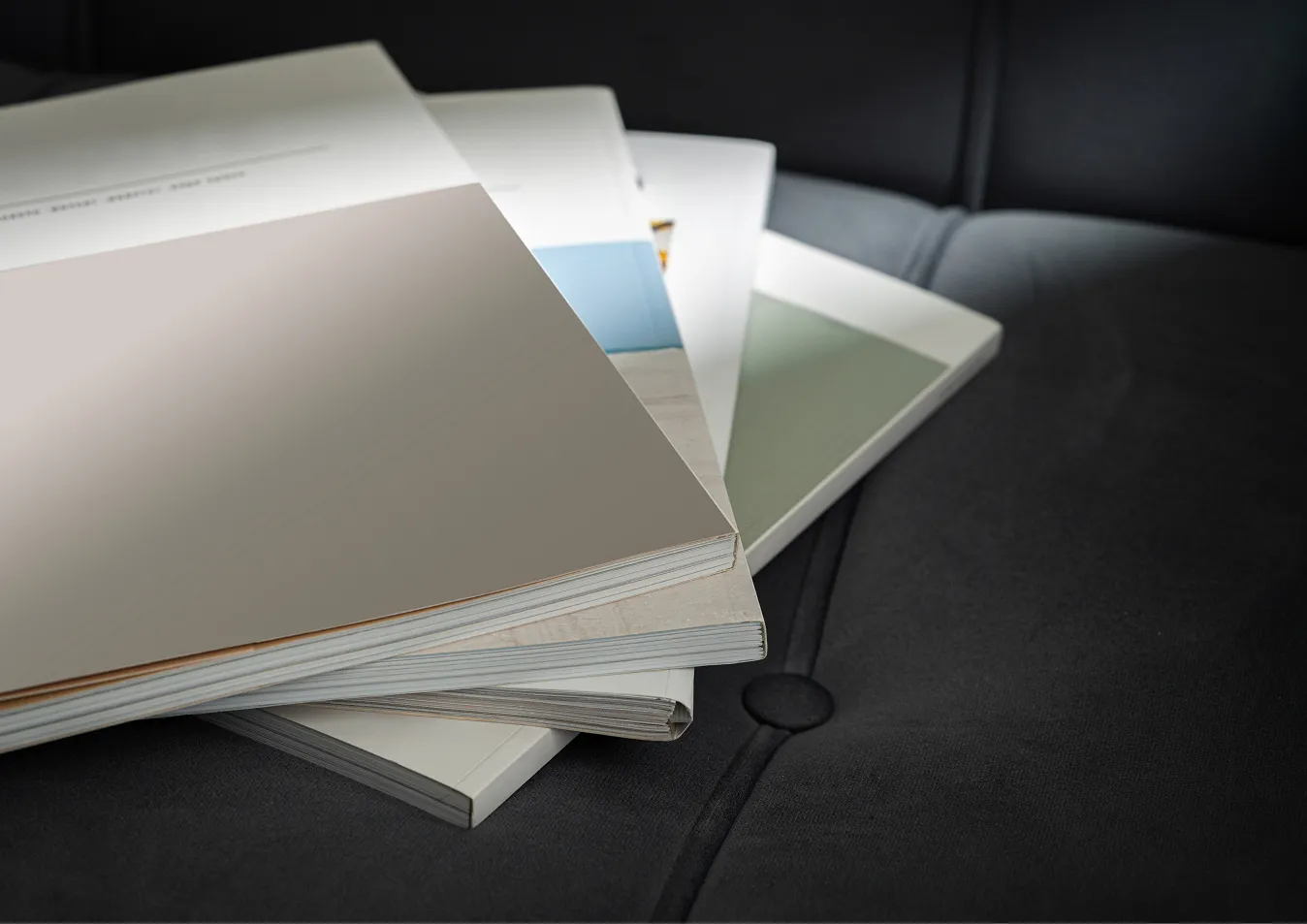 Ein Stapel von geöffneten Zeitschriften oder Katalogen liegt auf einem schwarzen gepolsterten Sofa.