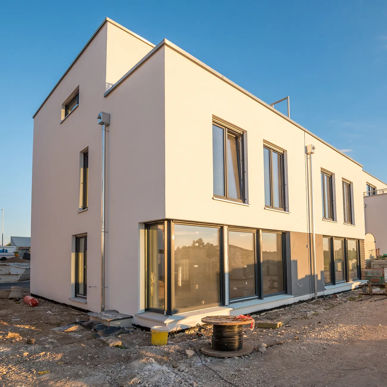 Modernes zweistöckiges Wohnhaus mit großen Fenstern in einer Baustelle bei Sonnenuntergang.