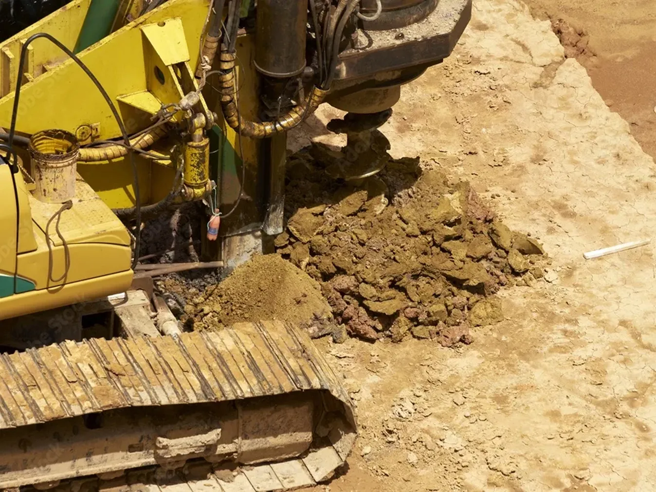 Gelbe Bohrmaschine mit einer großen Bohrschnecke, die Erde an einer Baustelle aushebt.