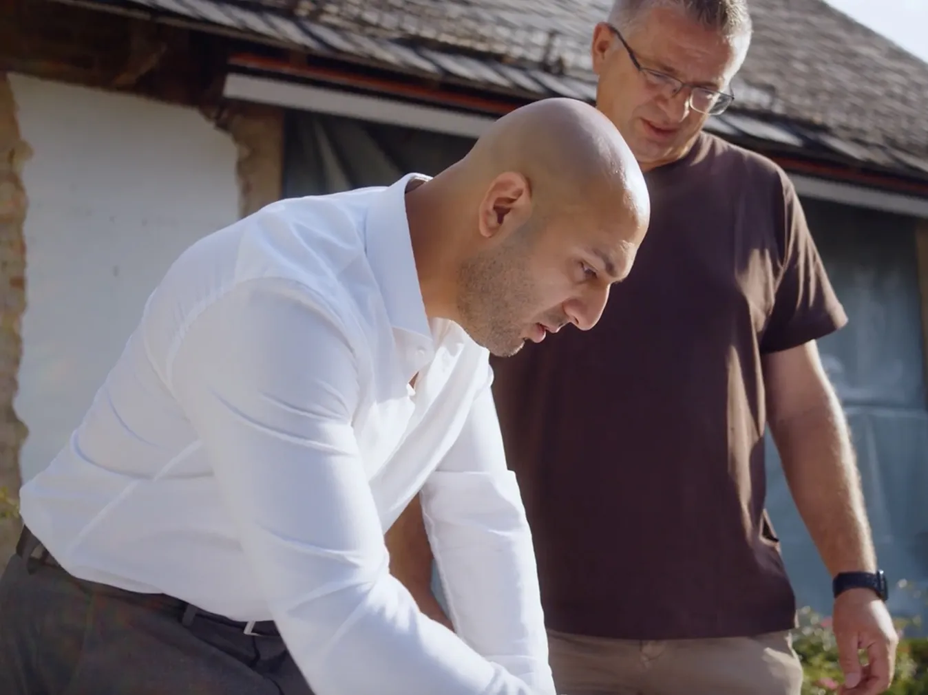Zwei Männer, einer in weißem Hemd und einer in braunem T-Shirt, blicken konzentriert auf etwas vor ihnen.