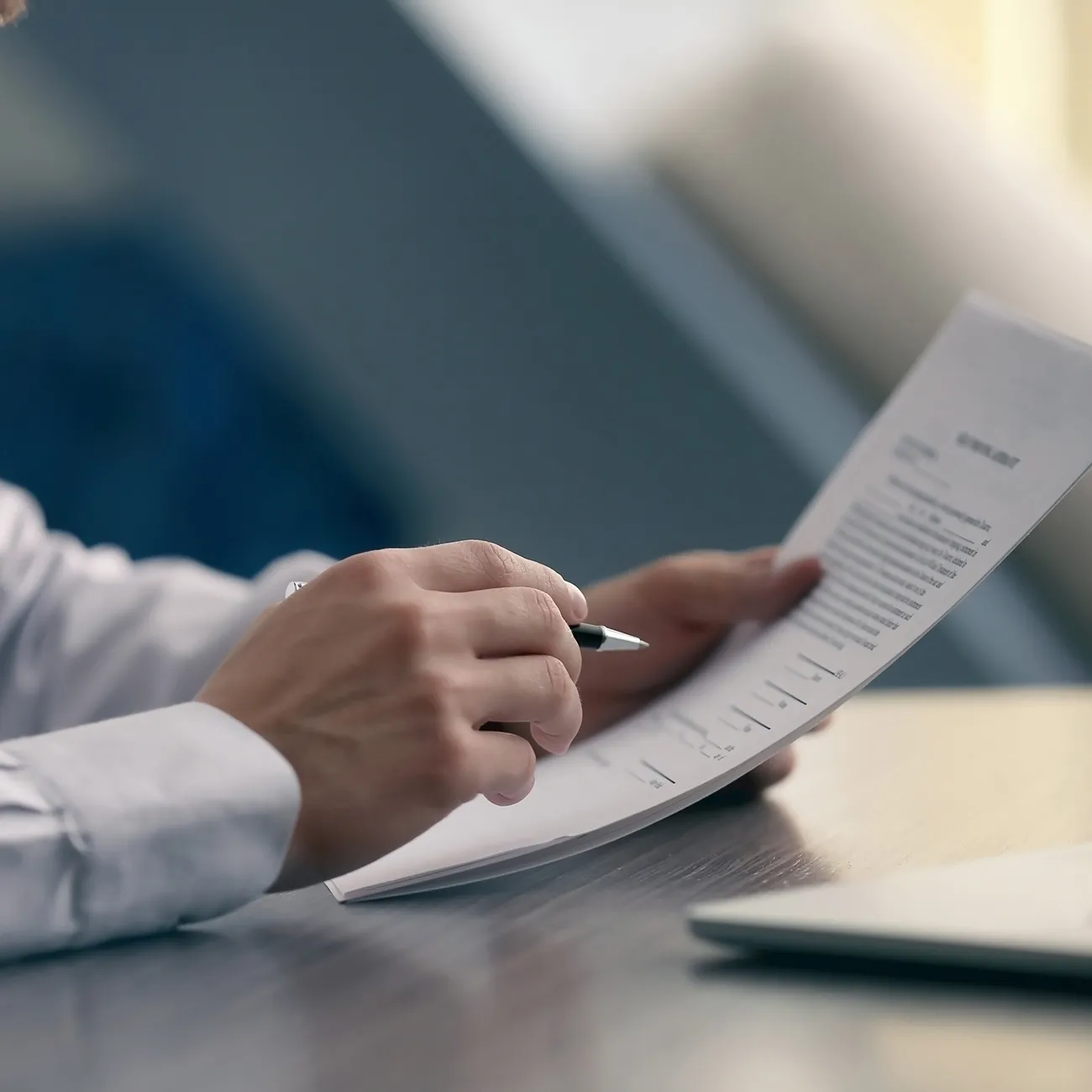 Person hält einen Stift und überprüft ein gedrucktes Dokument an einem Tisch.