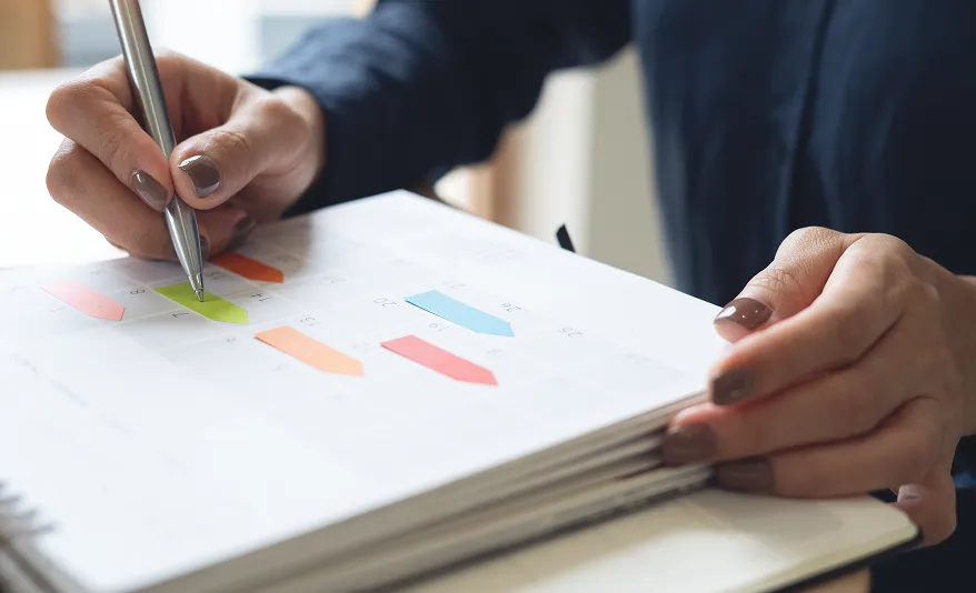 Person hält einen Stift und zeigt auf farbige Diagrammpfeile in einem Notizbuch.