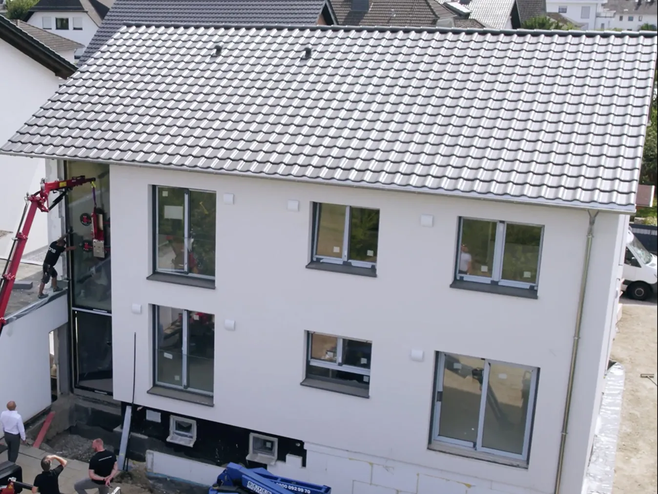 Zwei-geschossiges weißes Haus mit grauem Ziegeldach, an dem Bauarbeiter Fenster montieren.