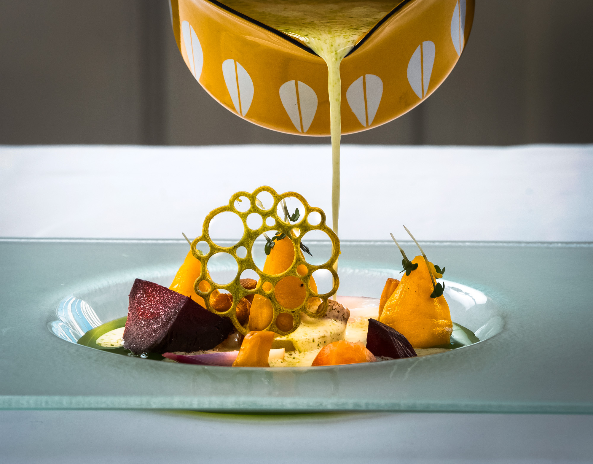 Saus helles over en gourmetrett med dekorative grønnsaker og en sirkel av crispy garnityr på en glasskål.