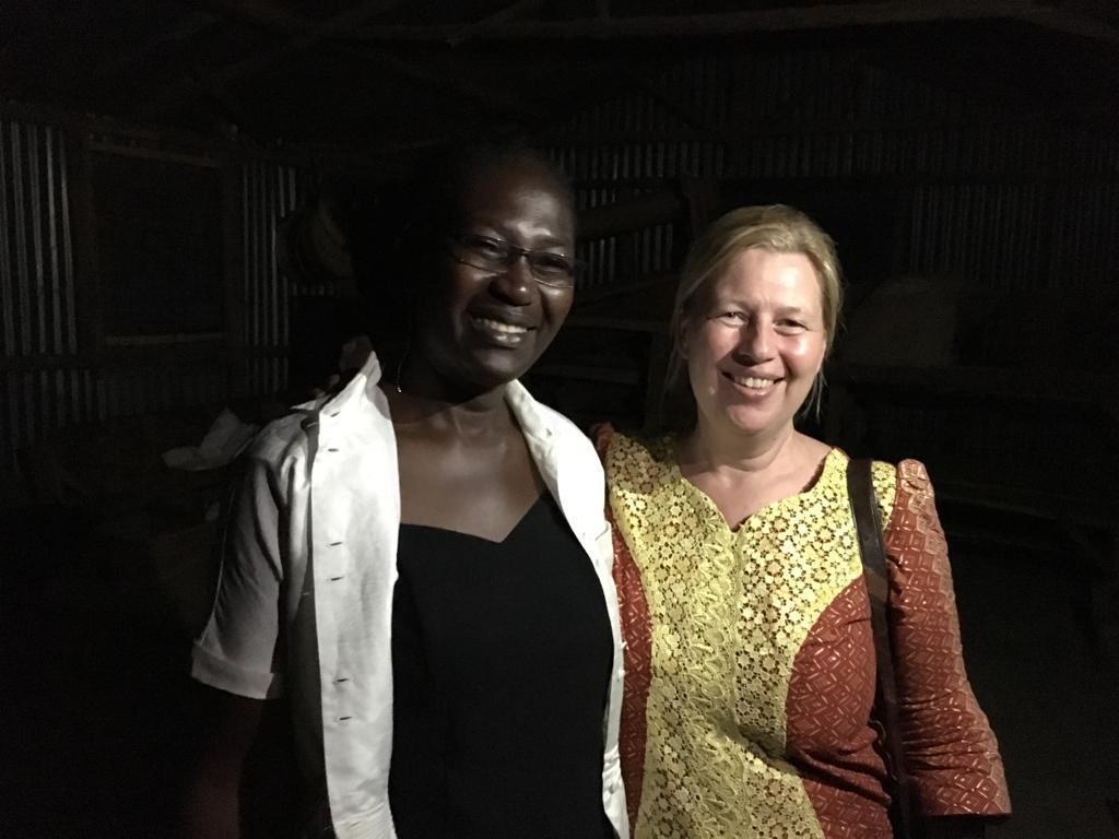 Two women smiling and standing close together in a dimly lit room with corrugated metal walls.