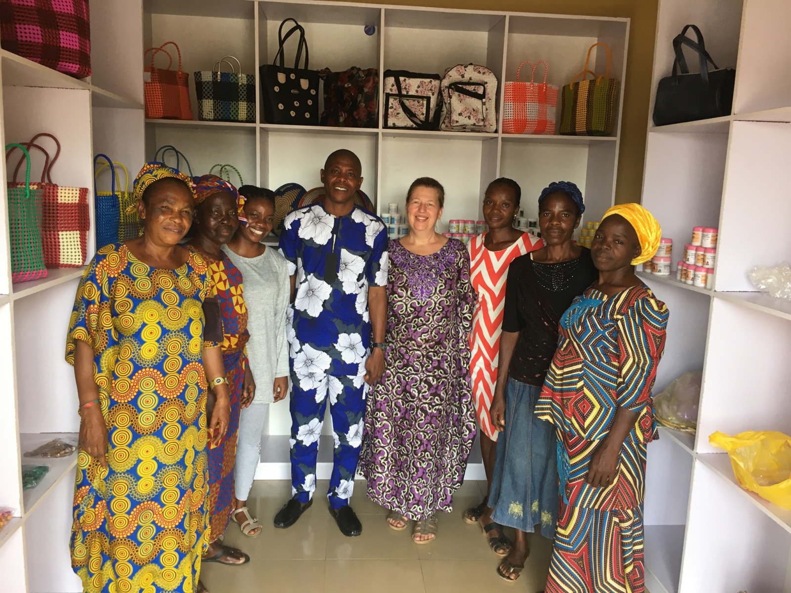 Group of eight people standing inside a shop with colorful woven bags displayed on white shelves.