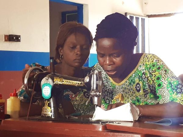 Two women focused on sewing fabric using a vintage black sewing machine indoors.
