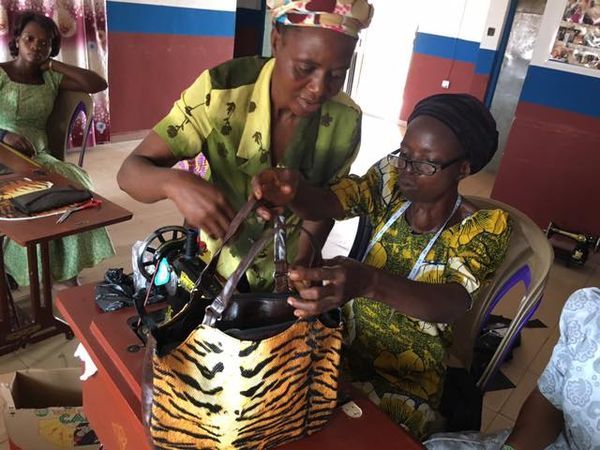 Two women closely examining a large tiger-print handbag in a room with seated people.