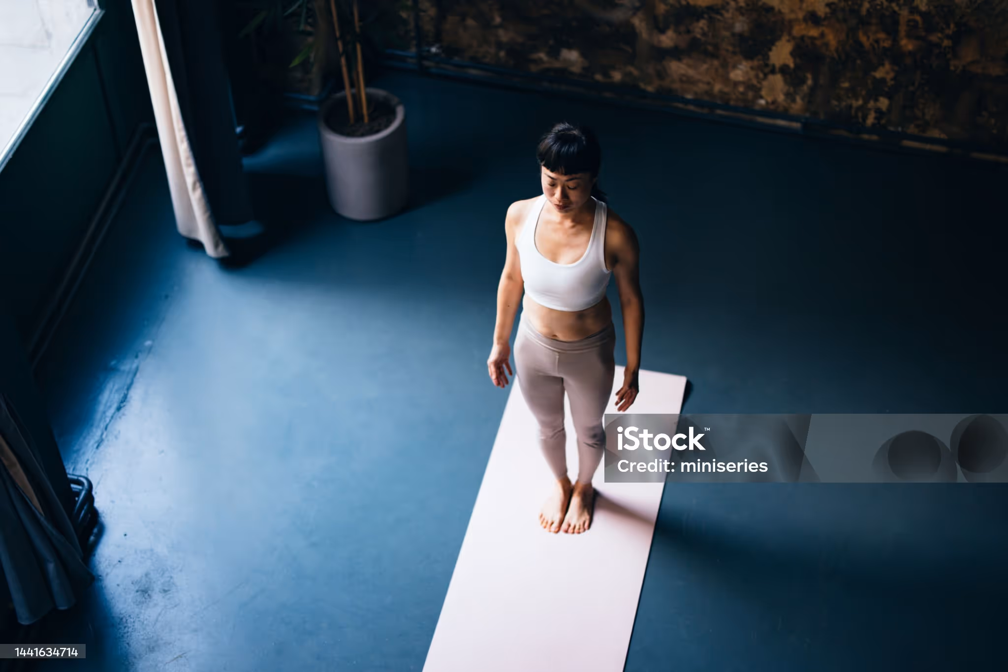 Woman standing on a yoga mat indoors with eyes closed, practicing mindfulness.