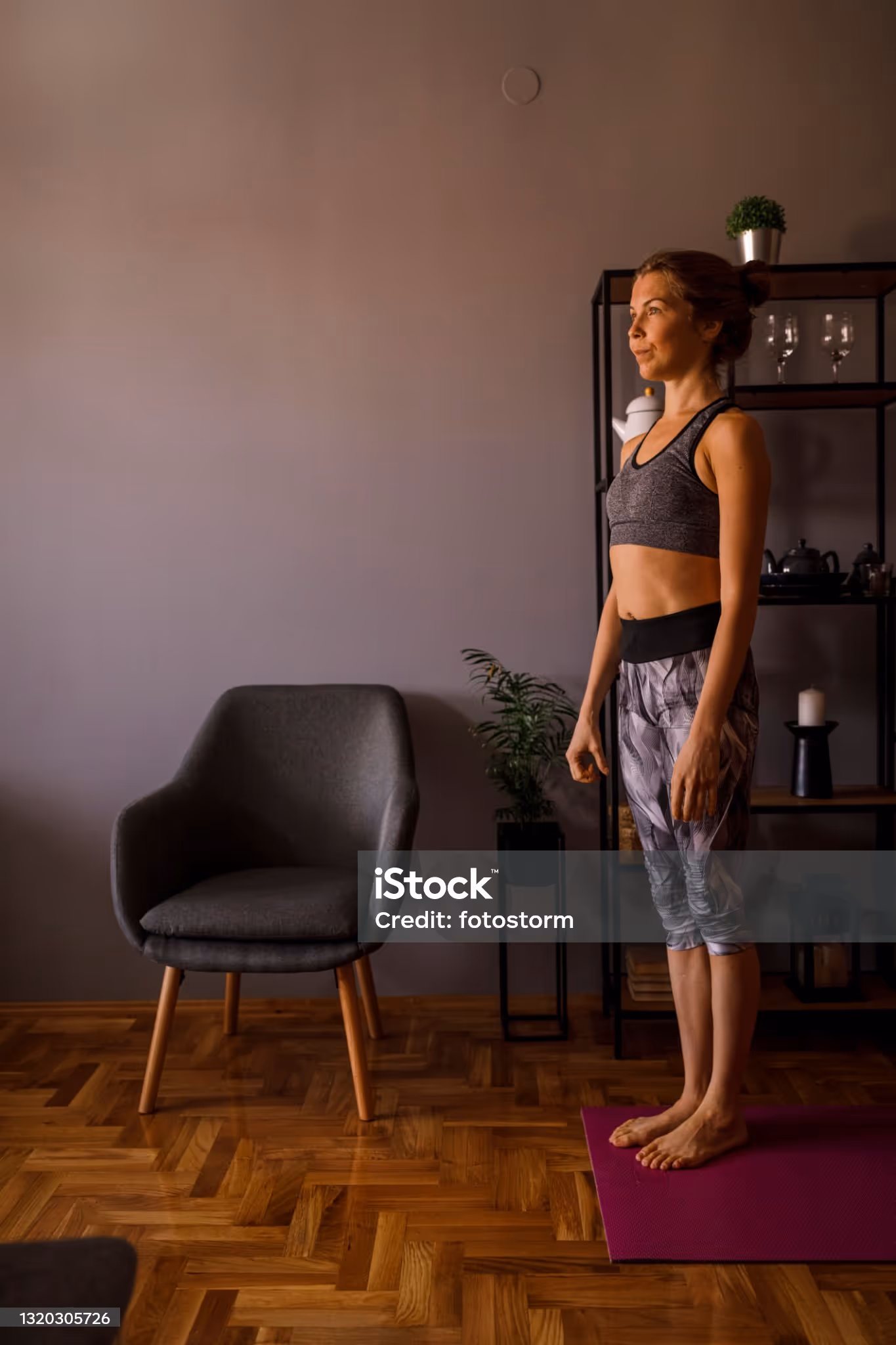 Woman standing on a yoga mat in a living room, preparing for exercise.
