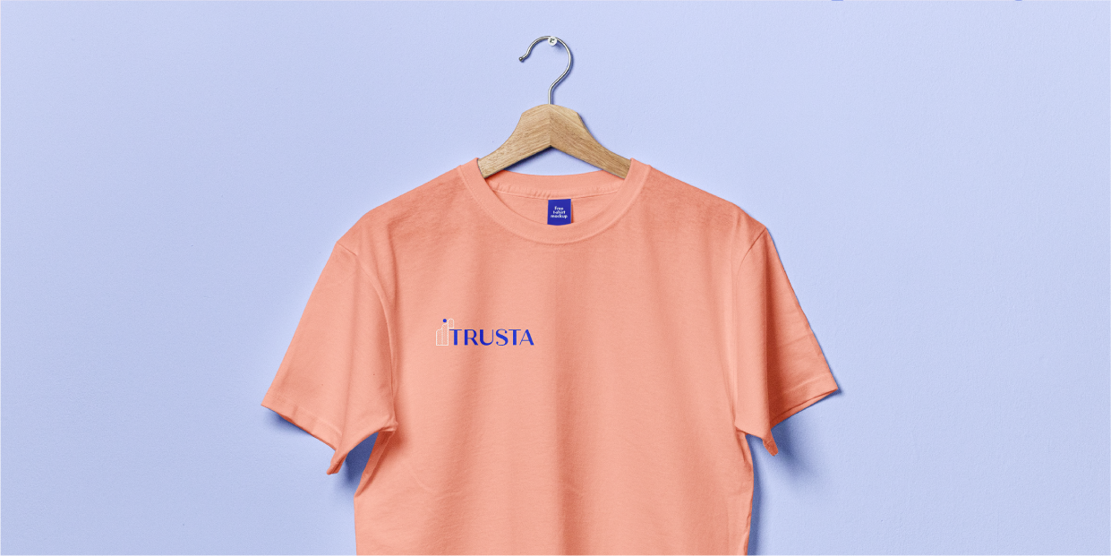 Mockup of a peachy shirt with the Trusta logo on the right side against a light purple background.