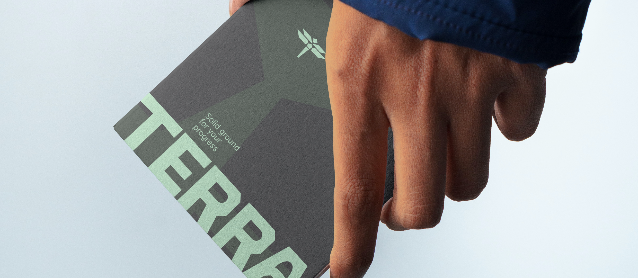 Mockup of a folder in terra bradning being held mid-air against a light background.