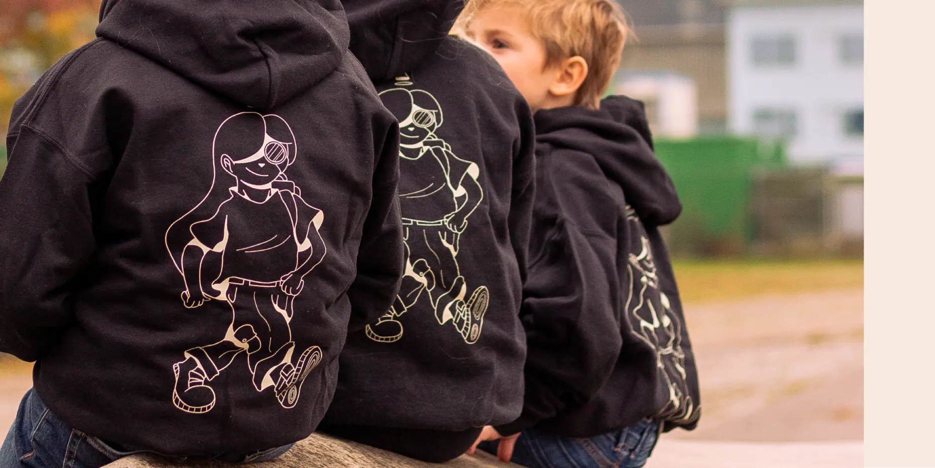 Zoomed in photo of 3 kids sitting next to each other wearing a branded Digitale Wolven black sweater shot of their backs.