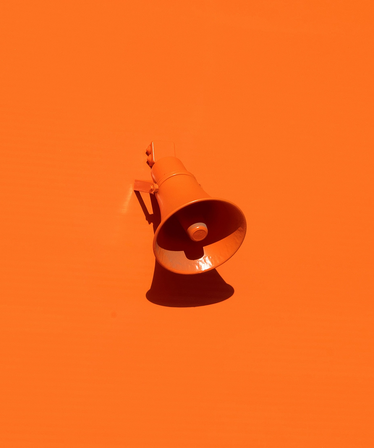 Orange megaphone mounted on an orange wall, casting a shadow against a monochrome background.