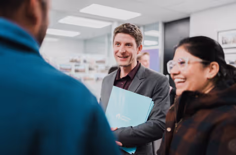 A Property Factory adviser smiling with a couple, holding a folder