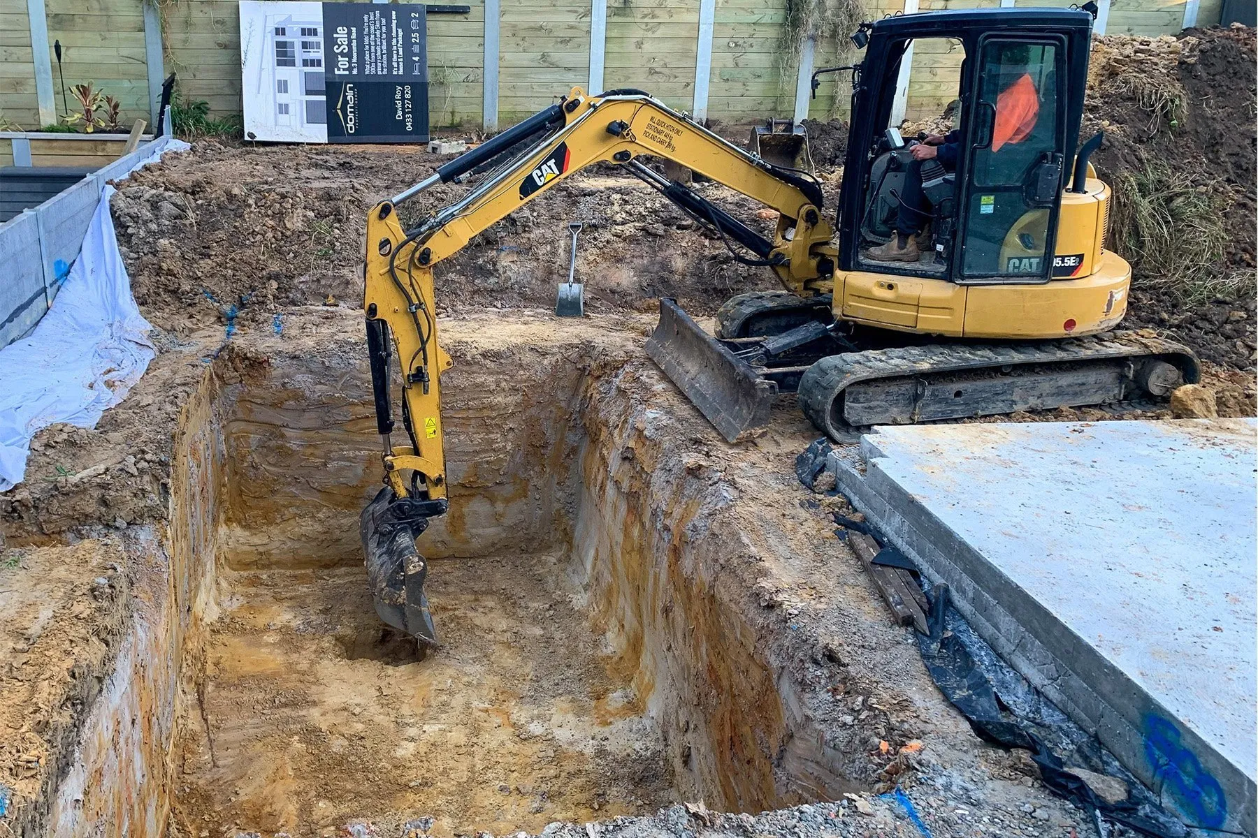 A homeowner and a contractor standing in a backyard looking at blueprints, pointing out the future location of the swimming pool digging site.