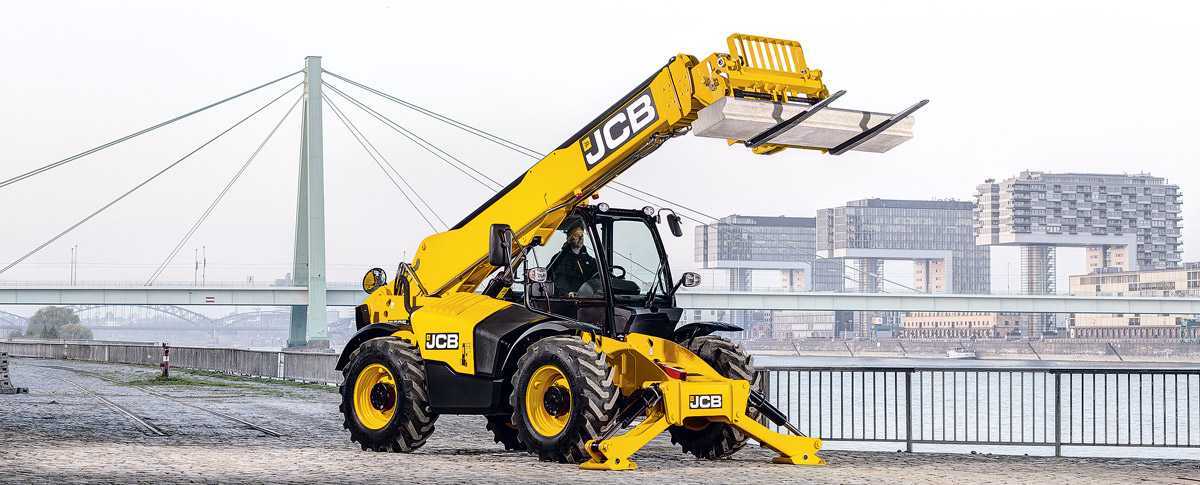 A heavy-duty telehandler with stabilizers deployed, performing safe lifting construction materials (steel beams) on a sloped site.