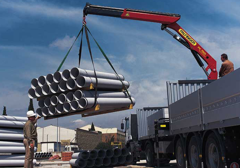 A telehandler acting as a material lift for construction site operations, placing a pallet of gypsum board through a second-story window opening.