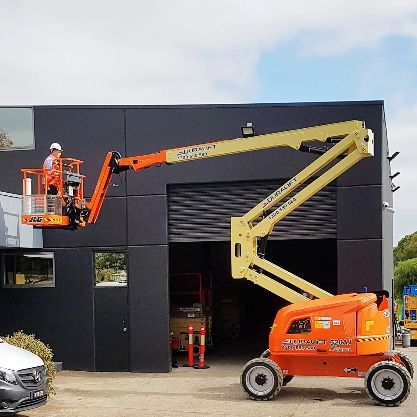 An articulating manlift hire unit bending its arm over a fence to repair a streetlight, demonstrating the "up and over" capability.