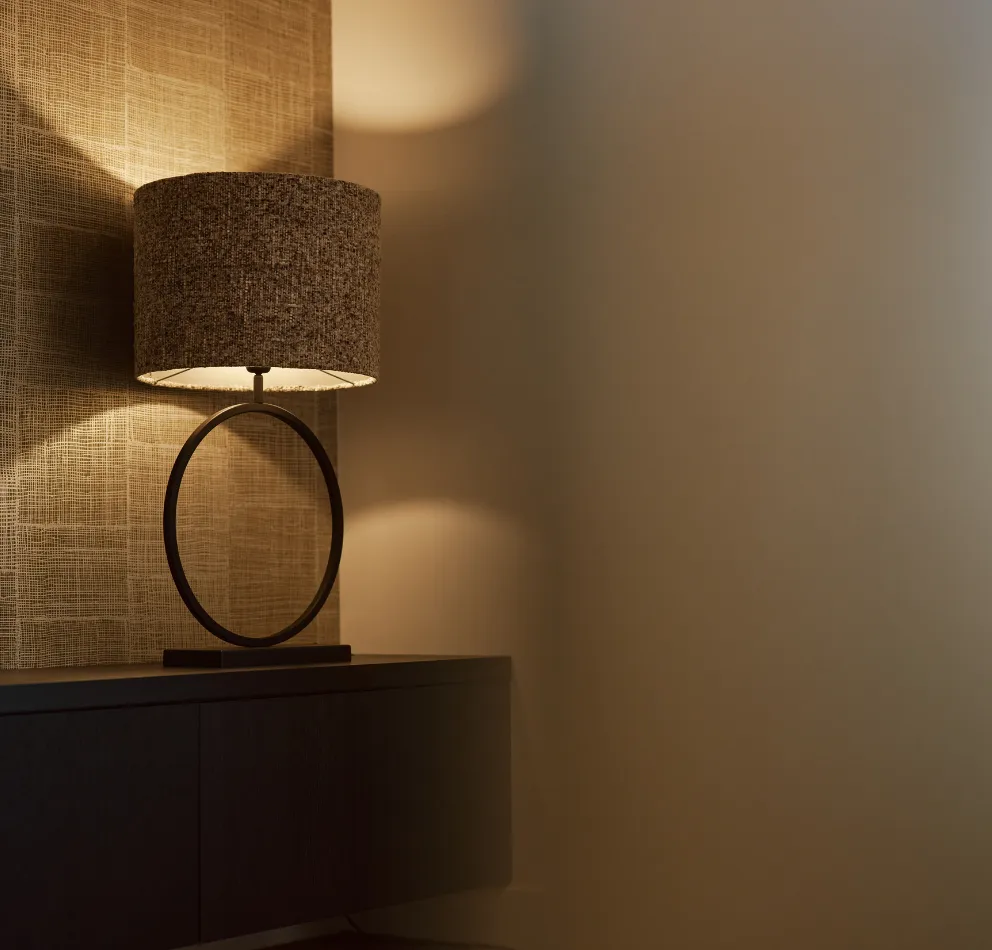 Moderne tafellamp met een cilindervormige kap en een ronde metalen basis staat op een kast tegen een muur met een gestructureerd oppervlak.