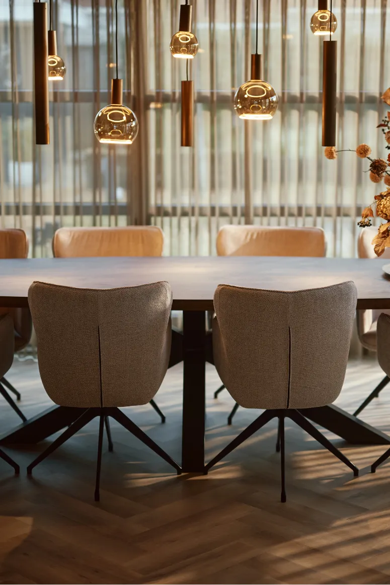 Moderne eetkamer met een grote houten tafel, zes beige gestoffeerde stoelen en hanglampen met glazen bollen.