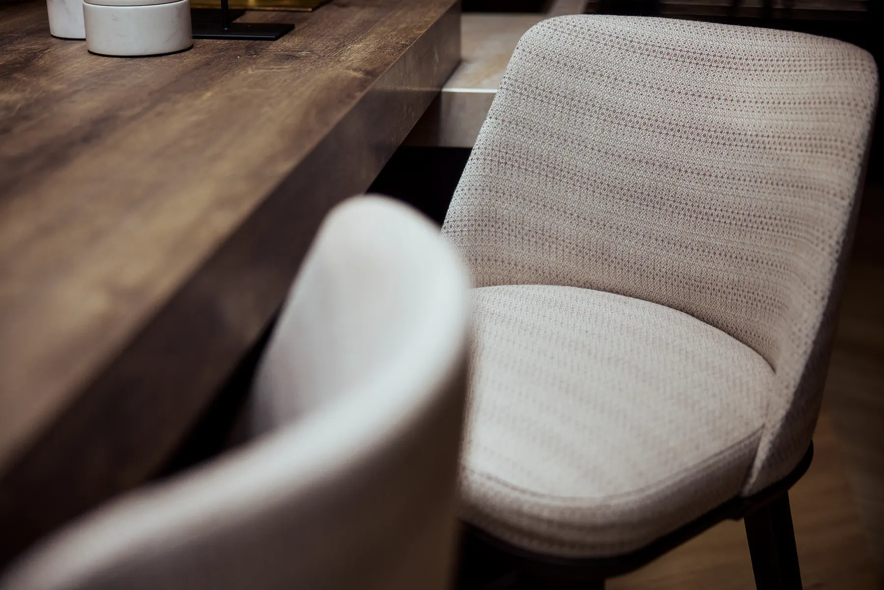 Close-up van een beige gestoffeerde eetkamerstoel naast een houten tafel.