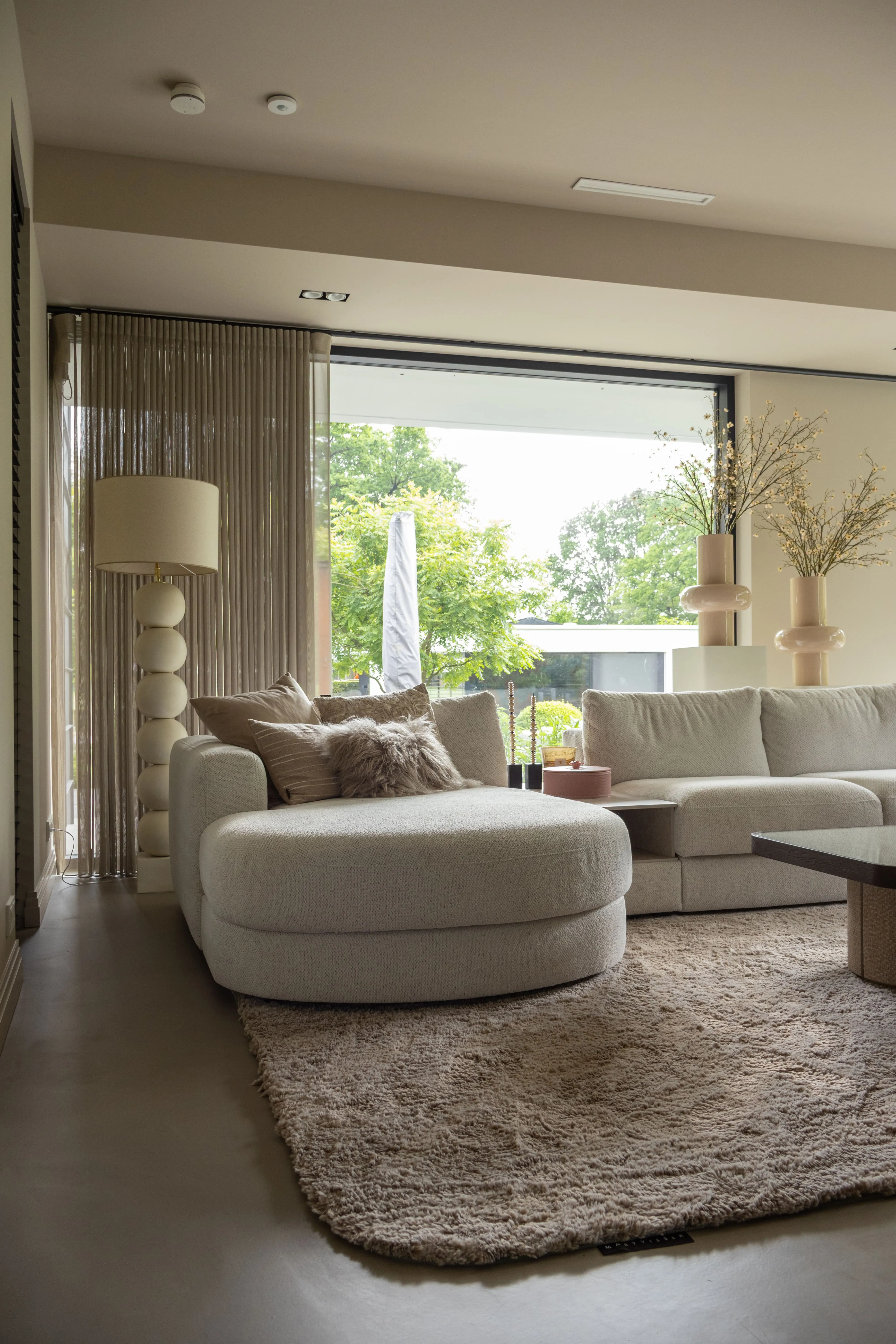 Lichte woonkamer met een moderne bank met ronde lijnen, zachte kussens in lichtroze en beige tinten en een comfortabel vloerkleed dat zorgt voor een warme uitstraling.