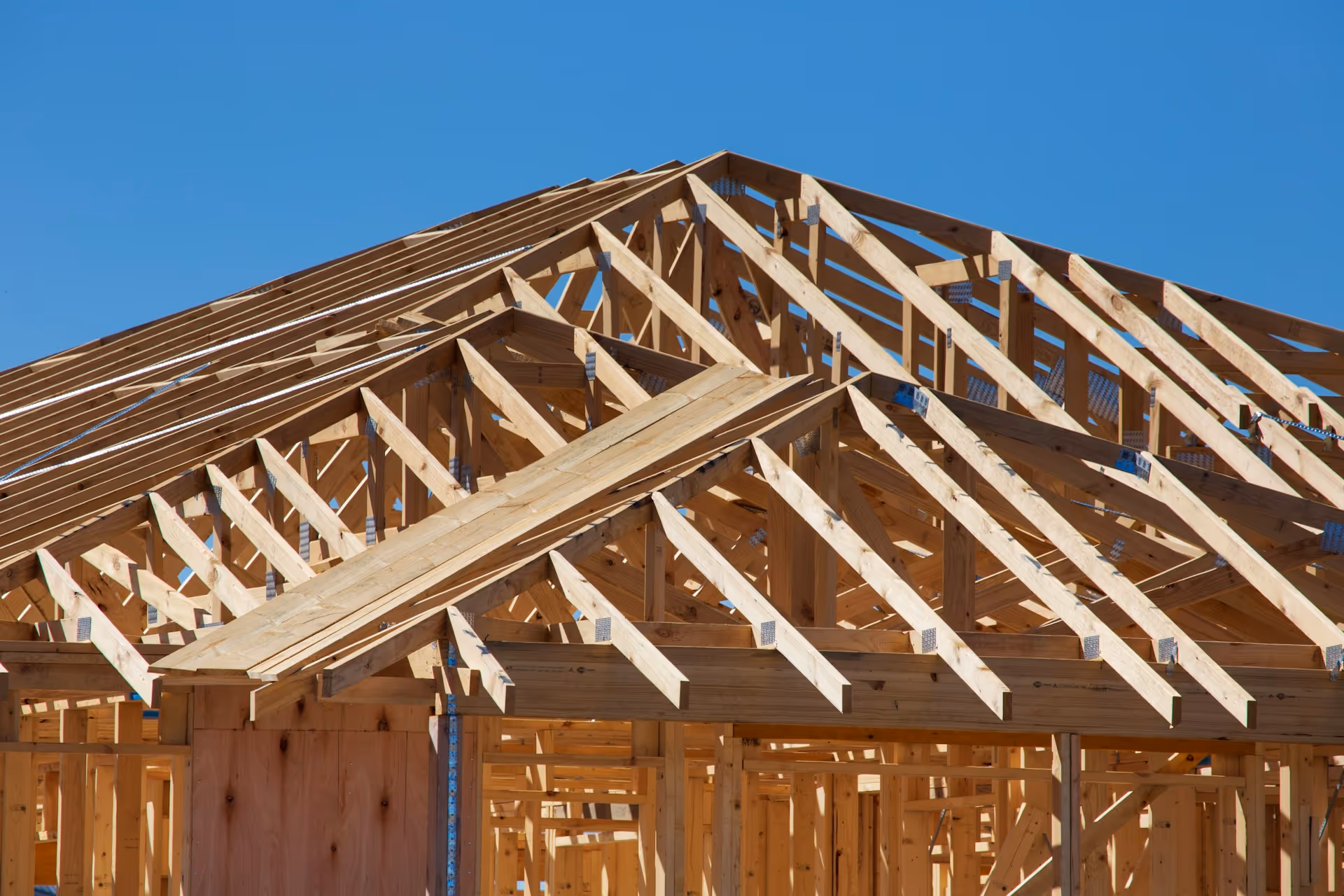Wooden roof framing structure under construction against clear blue sky.